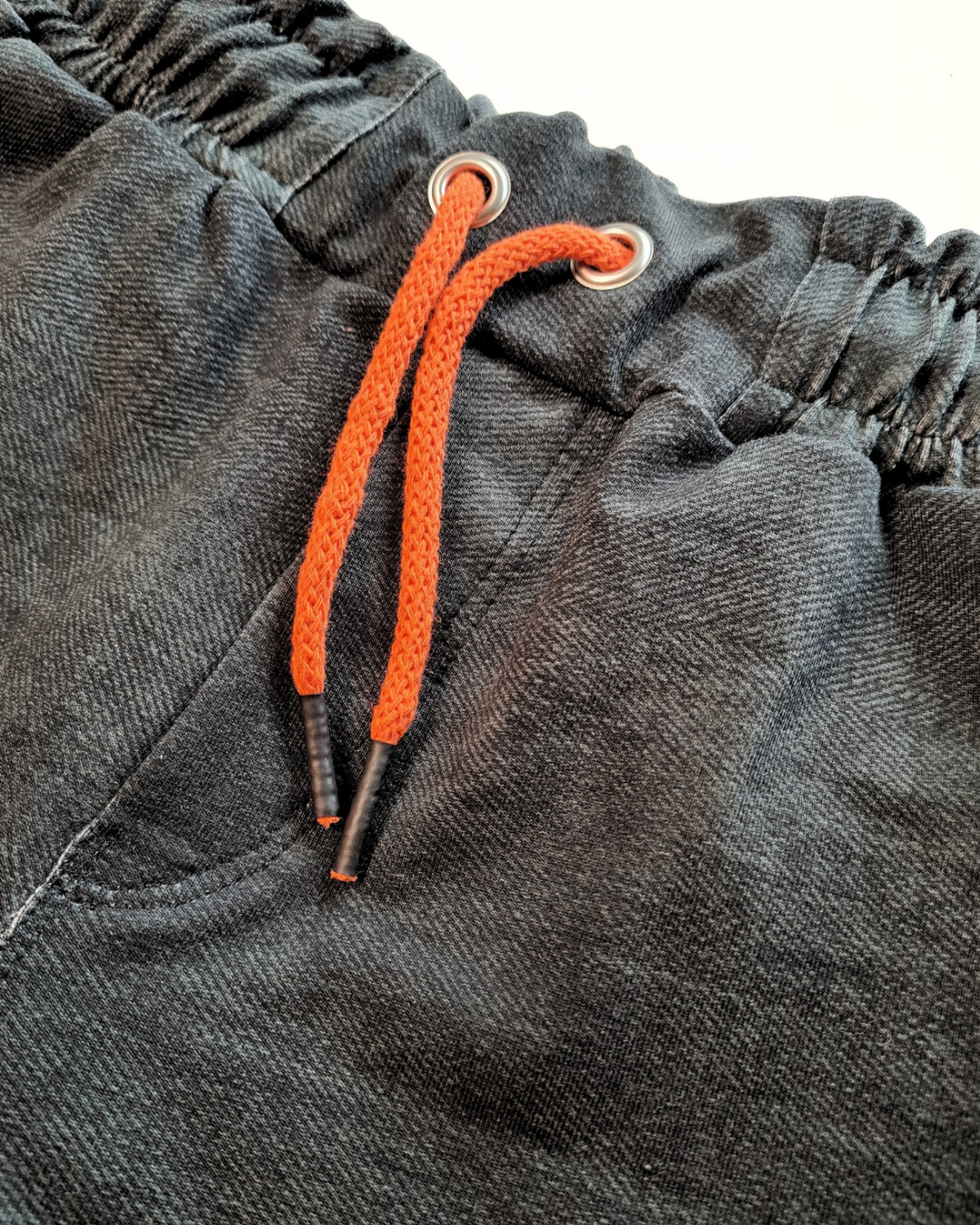 Nahaufnahme der schwarzen Jeans mit Gummibund und orangefarbener Kordel aus dem coolen Set für Jungs Gr. 116/122. Bequemer und moderner Look.