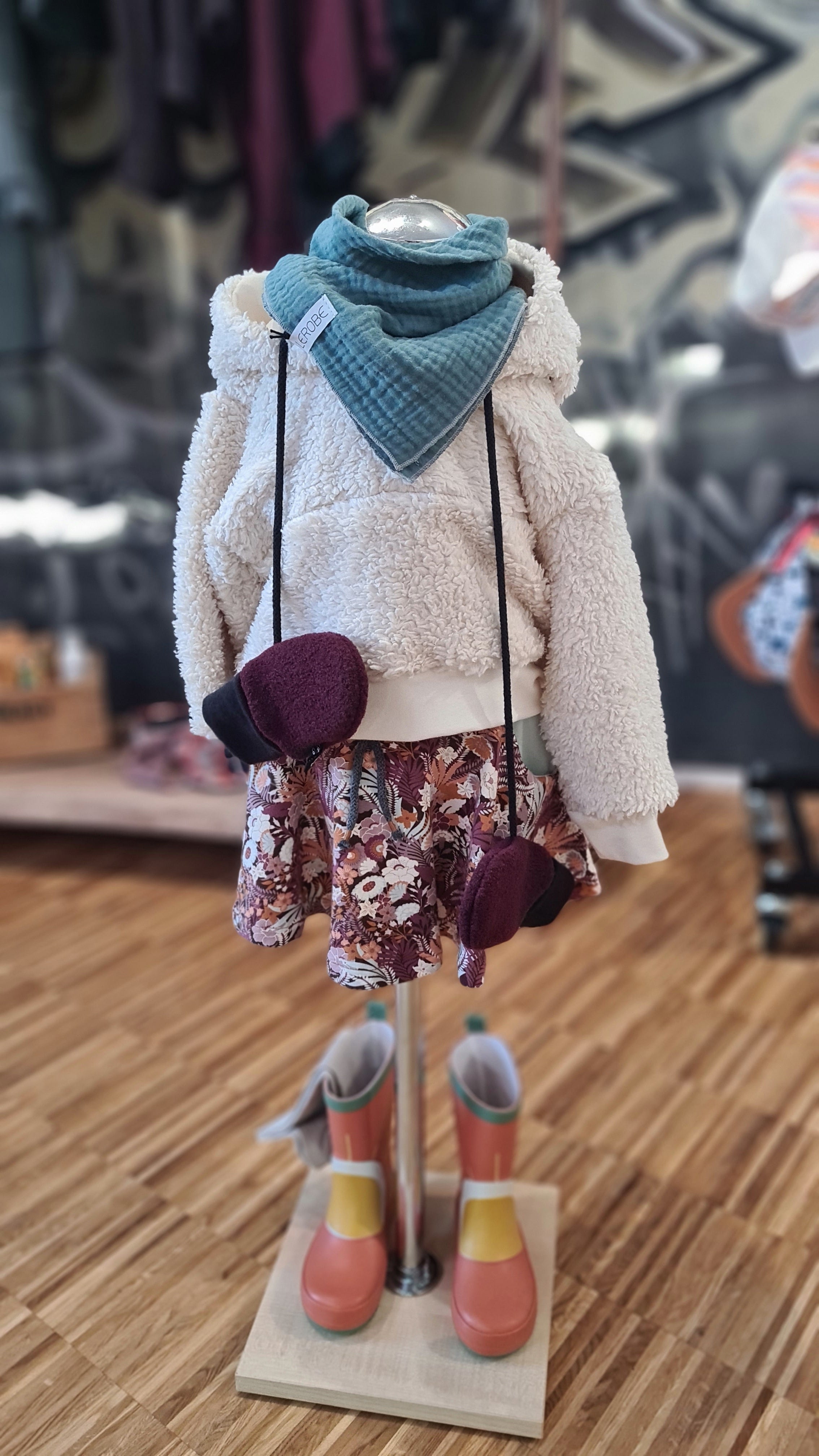 Bio-Baumwoll-Teddy Hoodie kombiniert mit Rock und Accessoires auf einer Schaufensterpuppe. Vielseitige, nachhaltige Kinderkleidung für stilvolle Outfits.